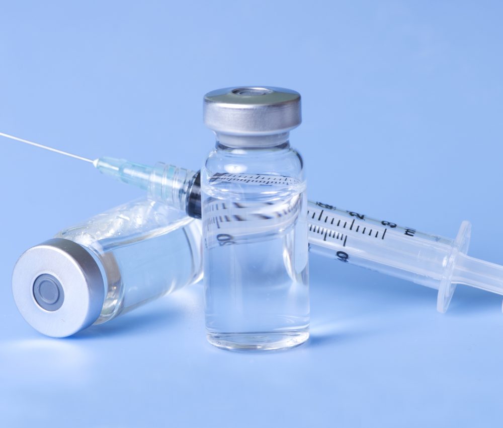 Syringe and vials of injectable medication on blue.